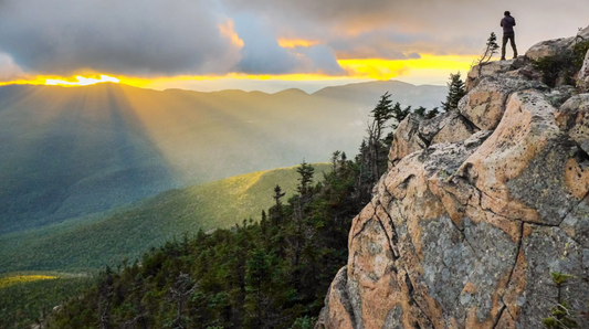 Person standing atop a mountain overlooking a valley. Blog. How to nurture our most fundamental relationship, Our relationship with our Body.