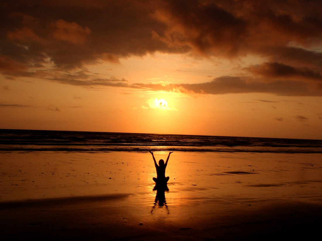 Person meditating at beach during sunrise. Benefits of meditation